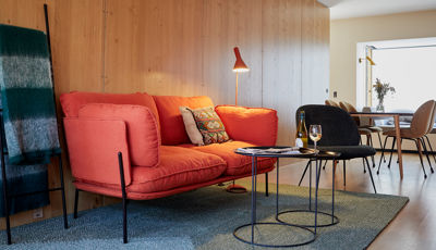 Stue med rød sofa og sorte sofaborde med spisebord i baggrunden ud til vindue med udsigt i 70 m2 hotellejlighed