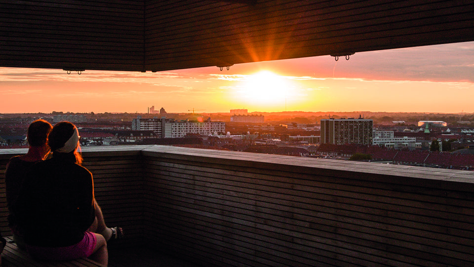 To mennesker nyder solnedgang over byen fra tagterrasse 