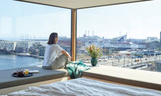 Kvinde sidende i sofa der nyder udsigten over Nordhavn med morgenmad og kaffe